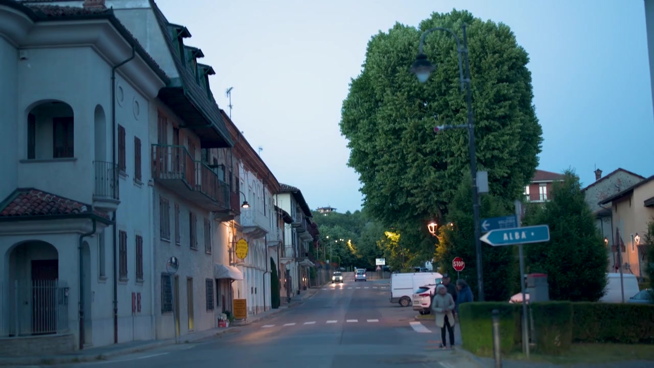 Slow forward tracking shot along a quiet village street at dusk in Piedmont, Italy.
