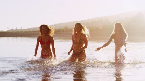 three female friends running and splashing in a lake