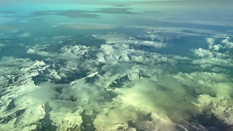 an elevated aerial view taken from a jet cockpit while flying with the sunrise light over the alps mountains covered by snow and few clouds.