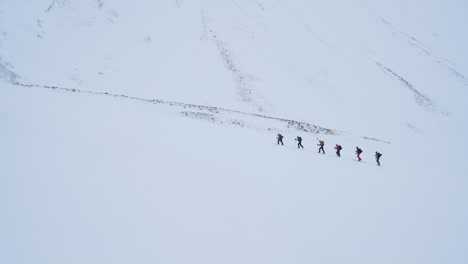 team of six hikers climbing snowy winter mountain in svalbard, handheld view