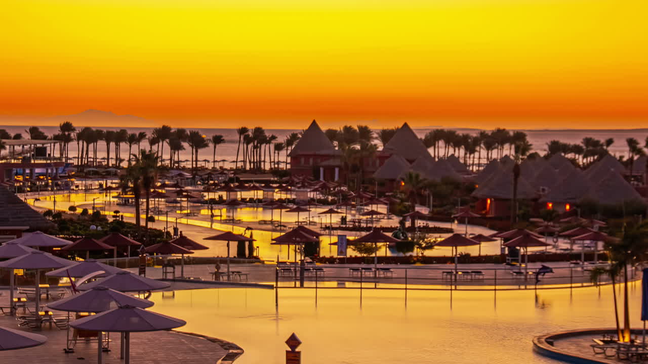Paesaggio aereo al tramonto: sfumature colorate e atmosfera dello skyline egiziano, con palme, piscina e lago lungo la strada costiera. Veicoli in transito e lago riflesso a Sharm El-Sheikh