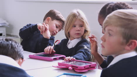 primary school children sitting at a table in a classroom with tablet computers, selective focus