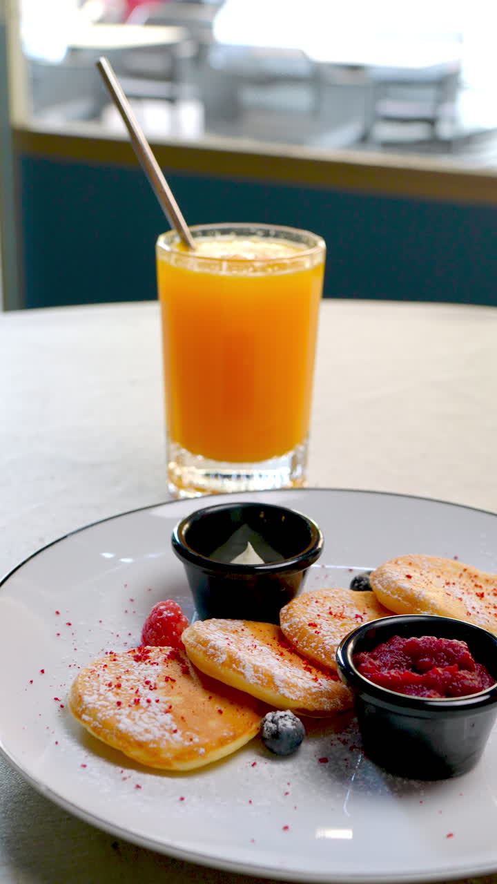 Traditional Eastern European quark pancakes featuring golden brown syrniki plated with vibrant berries, creamy sour cream, sweet jam, accompanied by freshly squeezed orange juice