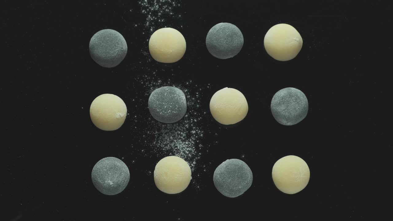 vista superior de panes oscuros y claros sobre fondo negro. harina o azúcar en polvo cae sobre la confitería. postre daifuku mochi. dulces tradicionales japoneses