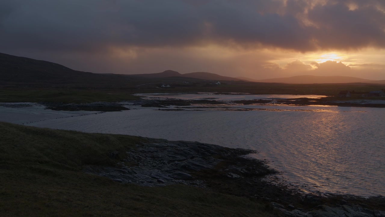 Golden hour shot of a winter sunrise during a rain storm over the island of North Uist. Clouds blow past in the wind as the tide comes in. Filmed near Lochmaddy on the Outer Hebrides of Scotland.