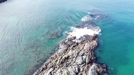 Overhead-aerial-drone-of-rocky-outcrop,-blue-ocean-and-waves-in-Maitai-Bay,-Karikari-Peninsula,-Northland,-New-Zealand-Aotearoa