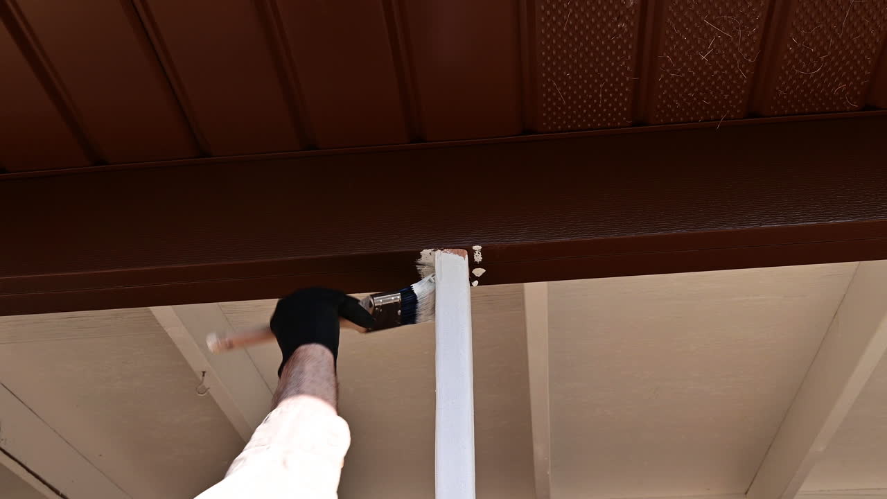 Operaio che applica primer bianco al legno all'aperto con un pennello.