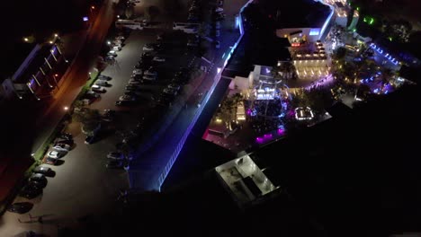 colorful lights at the luxurious party venue in algarve, portugal at night with cars parked at the parking area outside - aerial drone