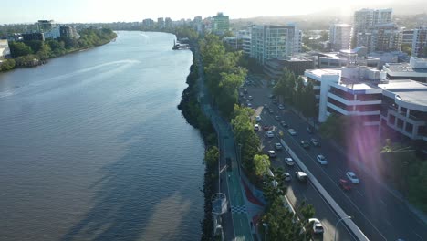 Vista-Aérea-Del-Hermoso-Río-De-Brisbane-Mientras-Vuela-Junto-Con-Esta-Toma-Panorámica-De-Drones,-Capturando-La-Unidad-De-Coronación-Y-Los-Senderos-Para-Bicicletas-Con-Mucho-Tráfico,-Con-Un-Impresionante-Destello-De-Lente-Por-La-Tarde