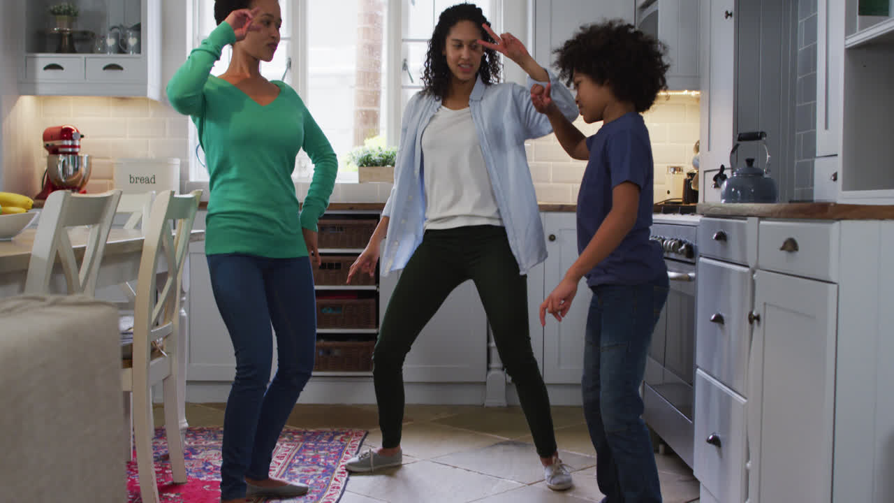 Mixed race lesbian couple and daughter dancing in kitchen