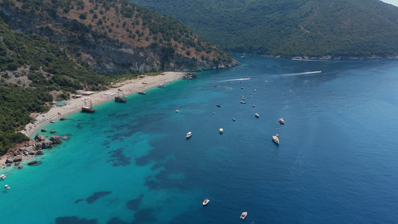 Boats anchored in the crystal-clear waters of a scenic beach along Albania's rugged coastline