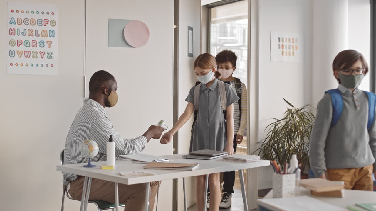 Male Teacher Measuring Students Temperature in Classroom