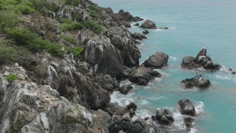 vista aérea en movimiento de las olas del mar del caribe golpeando las rocas en la orilla de una colina durante el día en st