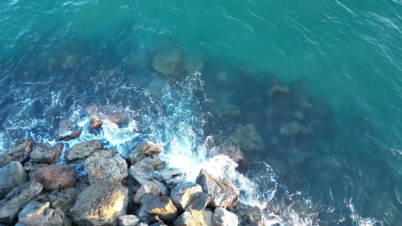 una vista aérea de un avión no tripulado olas chocando contra las rocas en una playa al atardecer