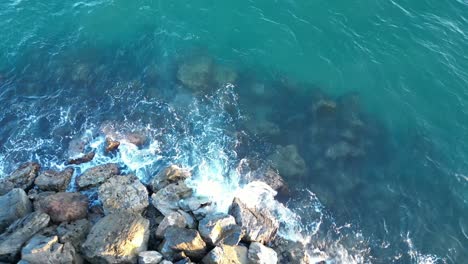 an aerial view from a drone waves crashing against the rocks on a beach at sunset