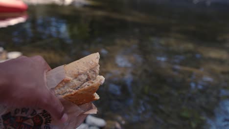 sosteniendo un sándwich - persona comiendo pan junto al río
