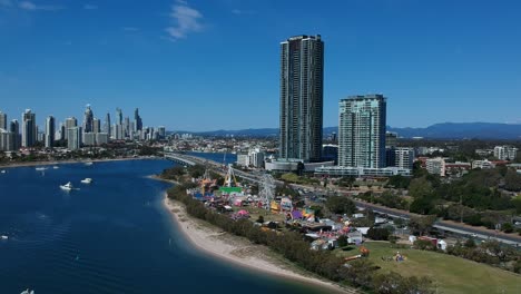 aerial view of a colourful carnival situated by the sea with a city skyline in the background