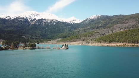 Drone-shot-over-a-lake-with-a-snowed-mountain-peak-in-the-background,-Greece