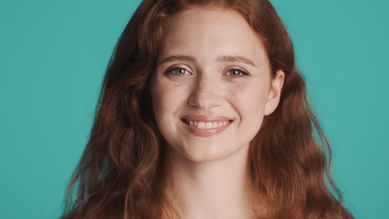 Redheaded girl in front of camera on turquoise background.