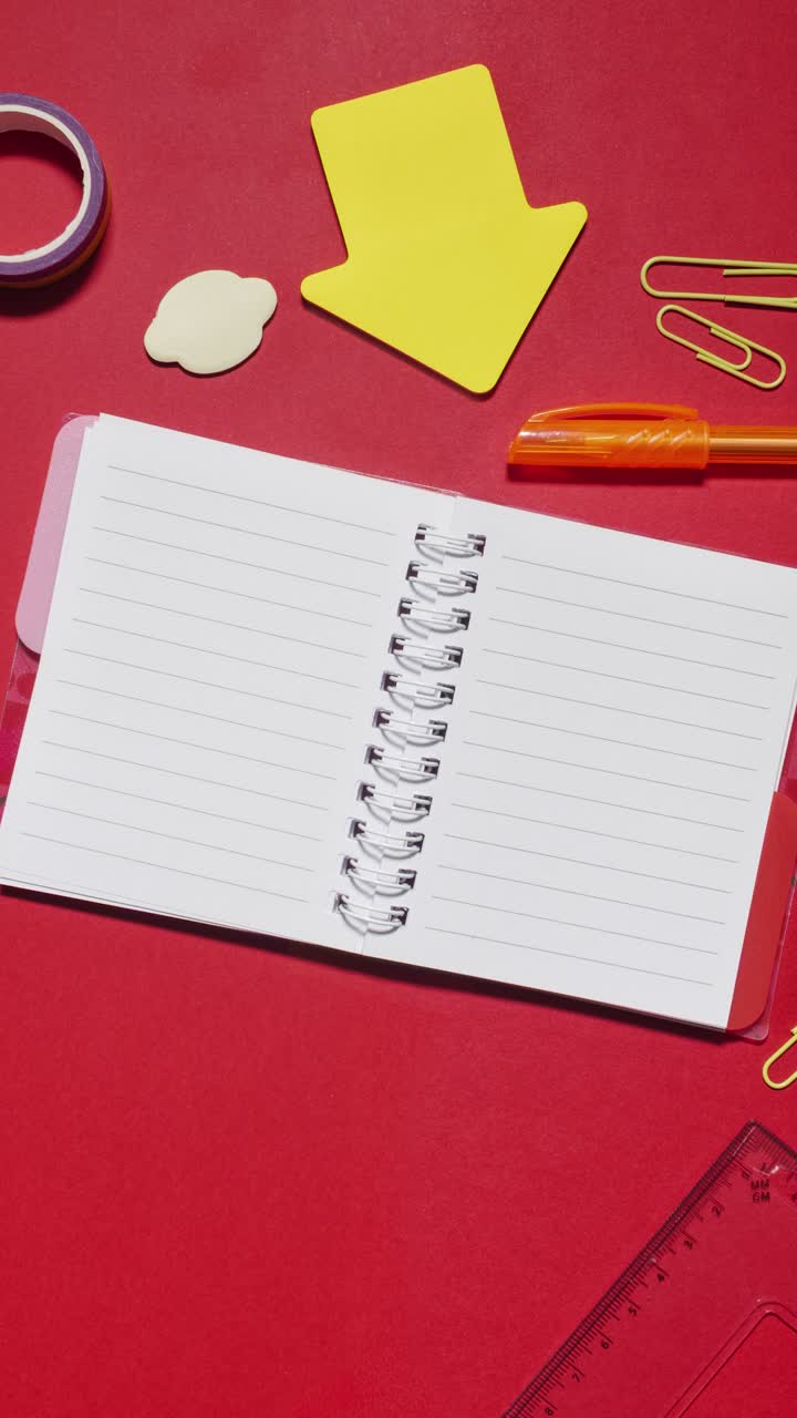 Stop motion supplies appear and vanish around spiral notebook that serves as copy space on red background