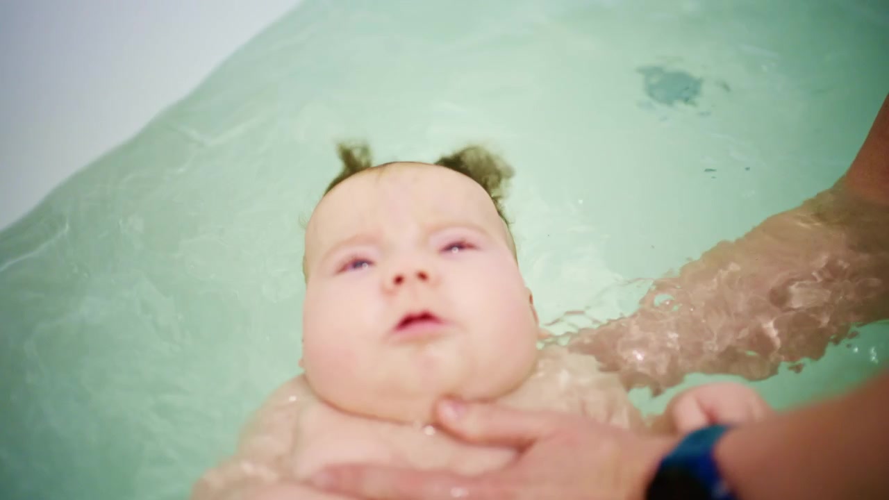 Close up of a baby supported by an adult during bath time