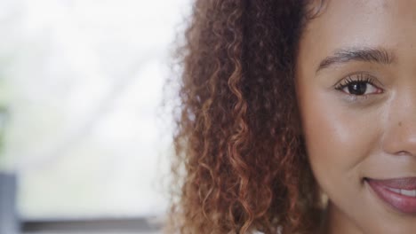 Half-portrait-of-happy-biracial-woman-with-curly-hair-smiling-at-home,-copy-space,-slow-motion