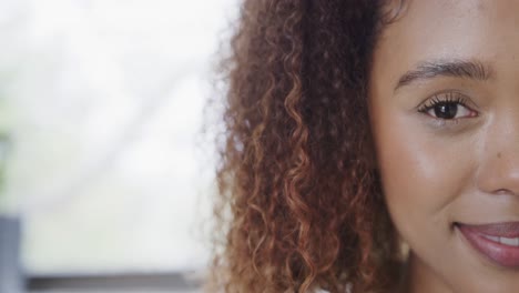 medio retrato de una feliz mujer biracial con cabello rizado sonriendo en casa, espacio de copia, cámara lenta