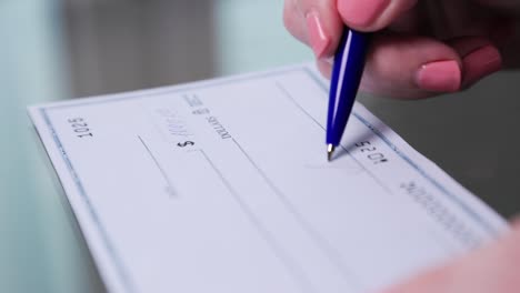 business woman hand signs and filling bank check for one thousand 1000 dollars