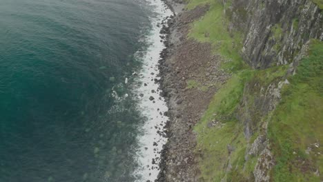 Drone-shot-from-above-of-coast-cliff-in-isle-of-skye-in-scotland,-clear-blue-water-and-green-grass