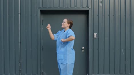 Female-nurse-wearing-medical-blue-uniform-dancing-happily-outside