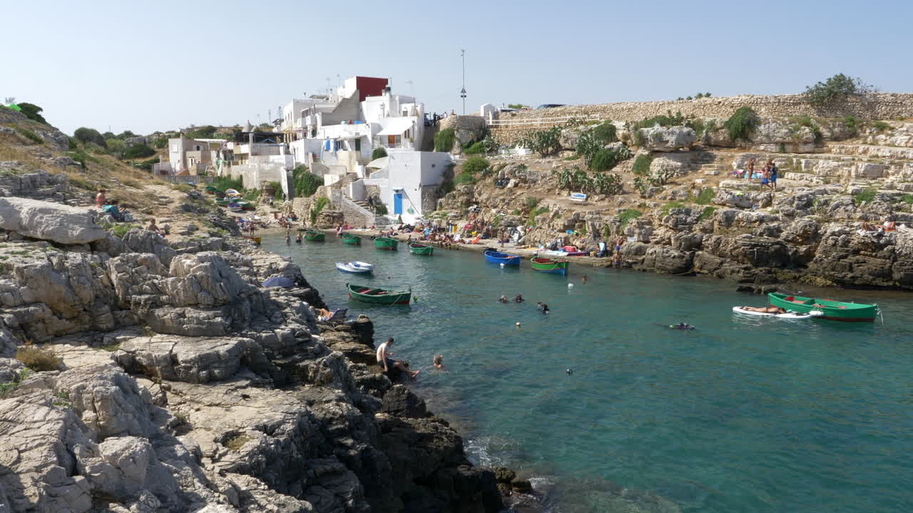 turistas nadando y tomando el sol en la playa de cala sala en port'alga, polignano a mare, italia