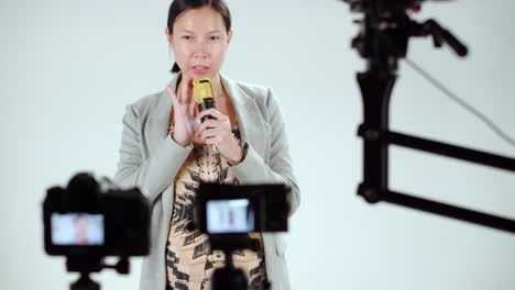 a female asian talk show host does a microphone test and sound check before recording her program - behind the scenes view