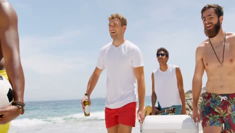 Mixed-race-male-friends-carrying-ice-box-on-the-beach-4k