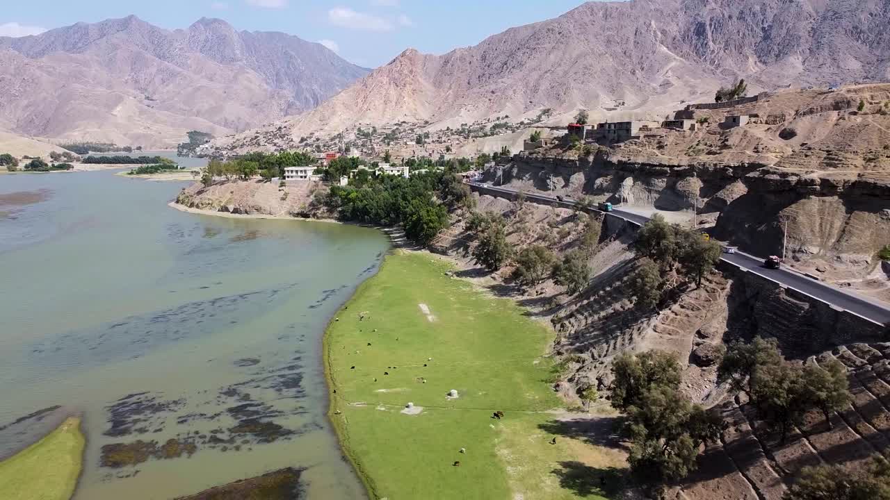 Aerial drone view of Kabul agriculture at river side, cows and farmer in a lush, rugged mountain valley in Afghanistan