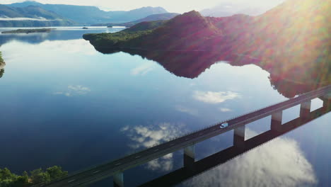 a large van is driving over a bridge with water reflections from the clouds and surrounding mountains on the west coast of tasmania in australia