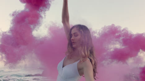 beautiful woman waving pink smoke bomb dancing on beach at sunrise celebrating creative freedom