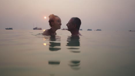 romantic couple swimming in the ocean at sunset