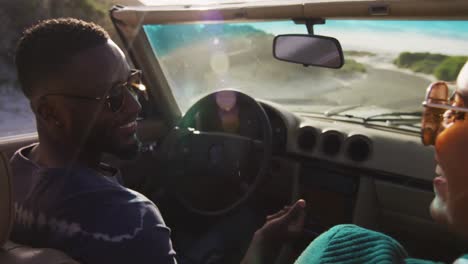 diverse couple driving on sunny day in convertible car looking at each other and smiling