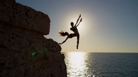 woman silhouette cliff jumping into ocean at sunset