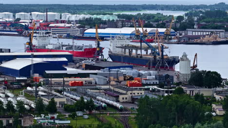 an industrial landscape view of the port of riga, showing cargo ships docked at ks terminal, alongside warehouses, harbor cranes, and adjacent chemical and gas storage facilities with rail access