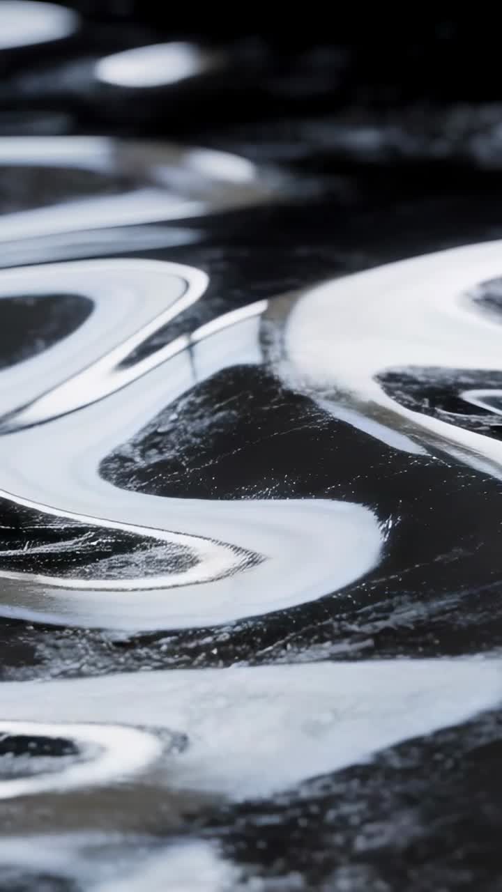 Vertical video: Rippling glossy surface during camera pan in studio, showing highlights and pools