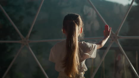 niño juega con el reflejo en la ventana en glamping. niña pequeña hace elegantes gestos de baile bajo la cúpula de vidrio en el hotel. niño activo en un hotel de lujo