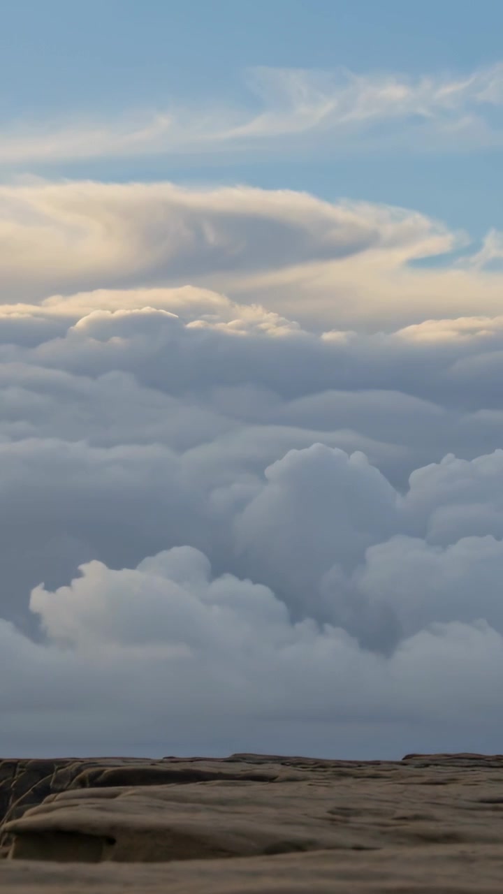 Vertical video: Billowing cloud bank shifting with sunlight moving over rocky ledge, anvil glowing