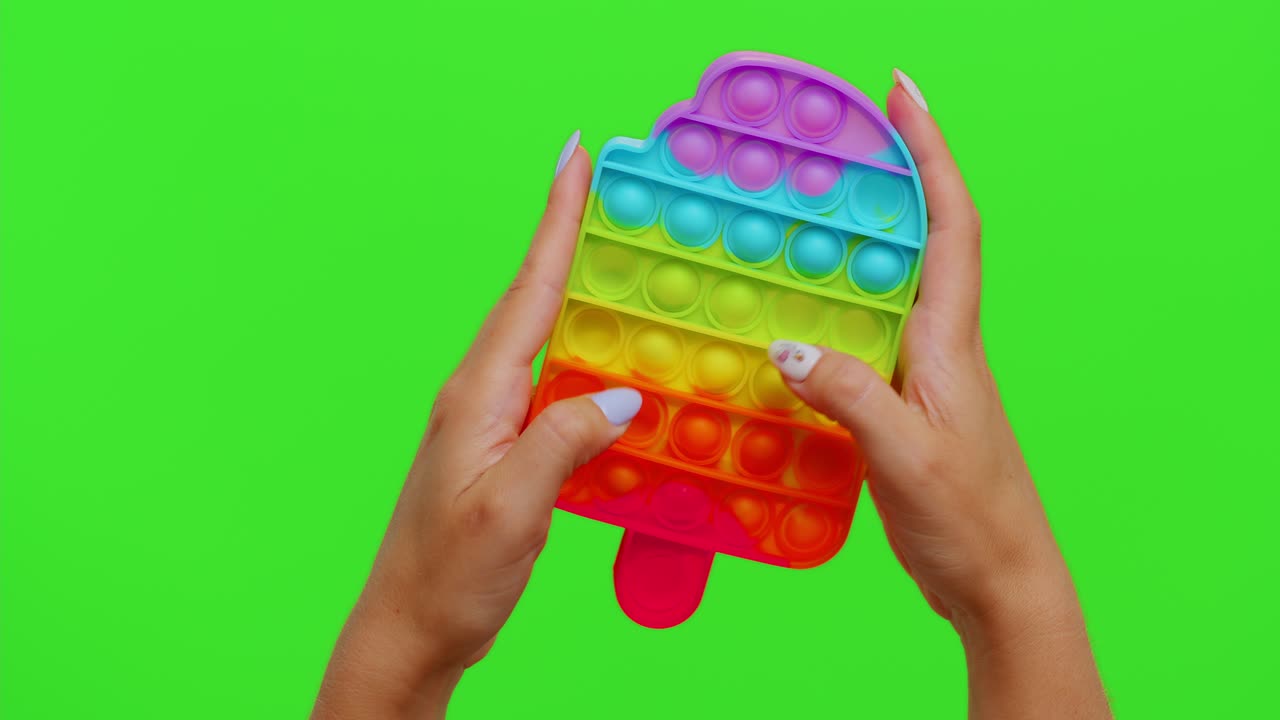 Kädet leikkivät sateenkaarenvärisellä pop it -fidget-lelulla.