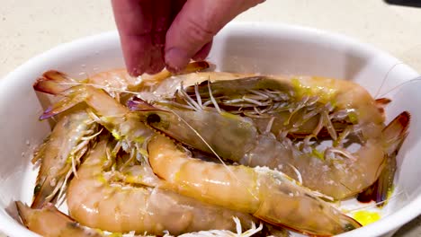 la mano salpica sal sobre los camarones frescos en el plato