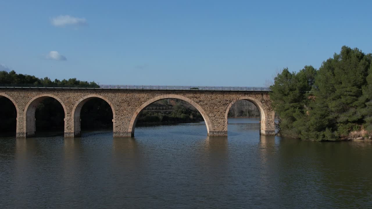 Aerial drone view flying over a reservoir and under a railway bridge in the afternoon light. El Reagajo. Castellon, Spain.