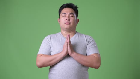 young handsome overweight asian man against green background