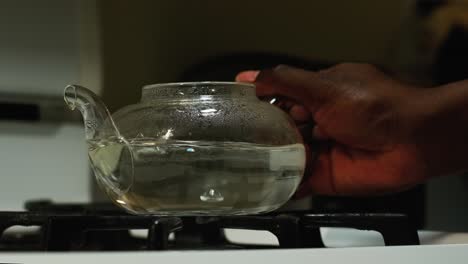 front view of an african american man taking a boiling glass tea pot off the stove