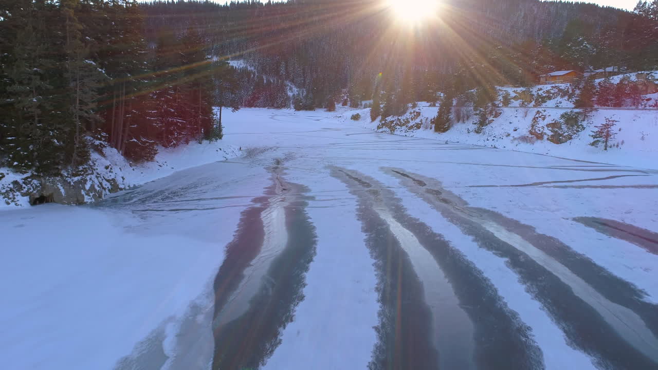 AERIAL: Flying above frozen lake with hills around it. Everything is covered with snow