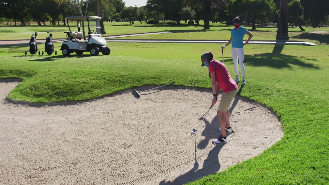 두 명의 백인 여성이 골프를 치고 얼굴 마스크를 쓰고  ⁇ 커에서 총을  ⁇ 고 있습니다.